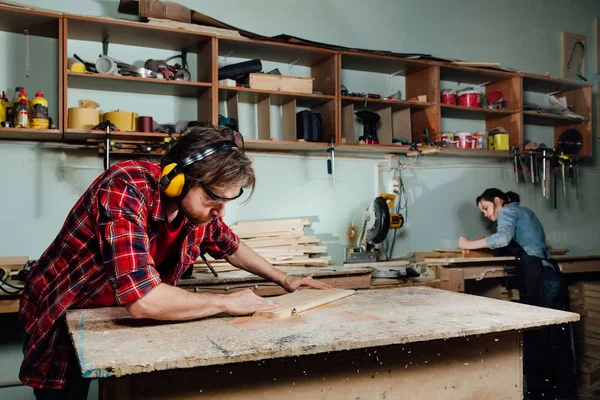 Deux menuisiers travaillent dur dans l'atelier. Un homme et une femme . — Photo