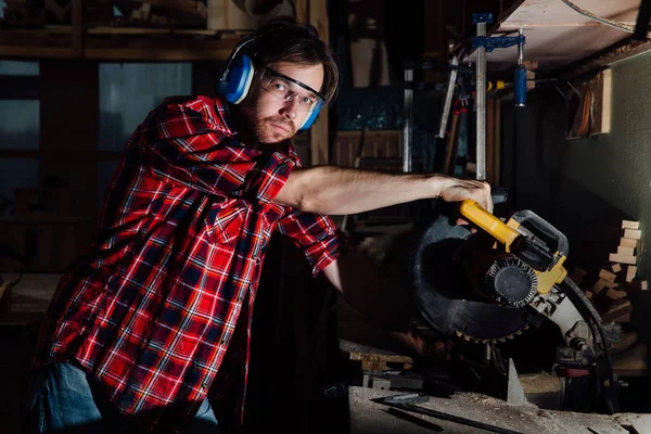 Brunette homme profession charpentier scies à bois avec une scie circulaire une planche en bois . — Photo