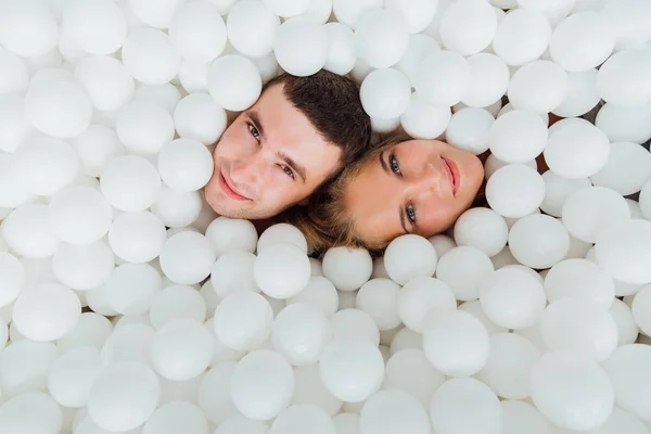 Couple d'amis aimants s'amusent entourés de boules en plastique blanc dans une piscine sèche . — Photo