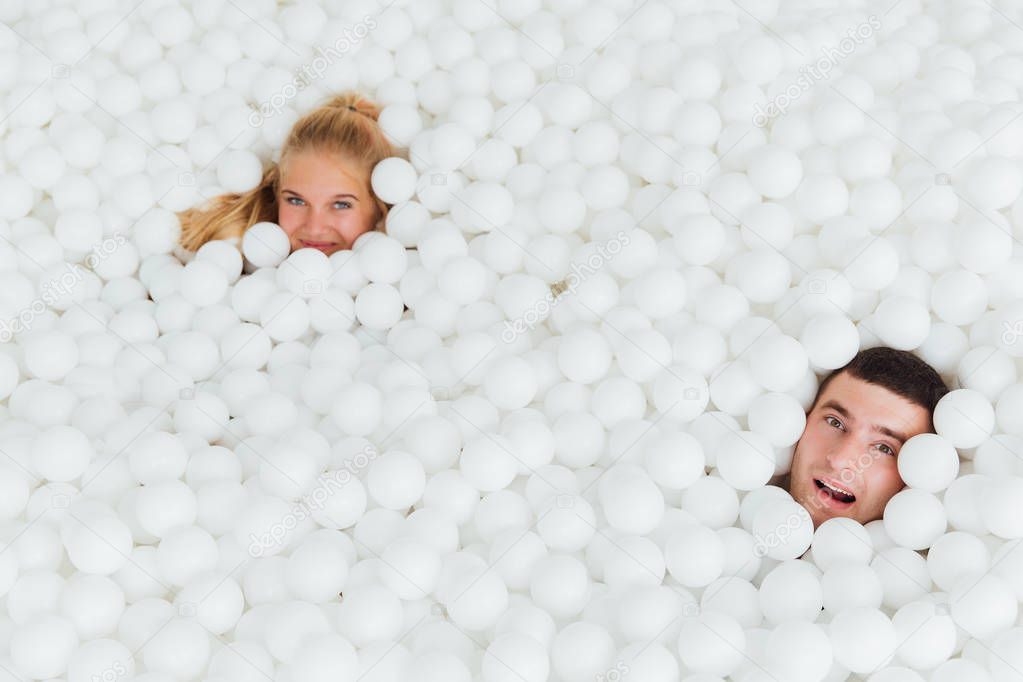 couple of loving friends have fun surrounded by white plastic balls in a dry swimming pool.