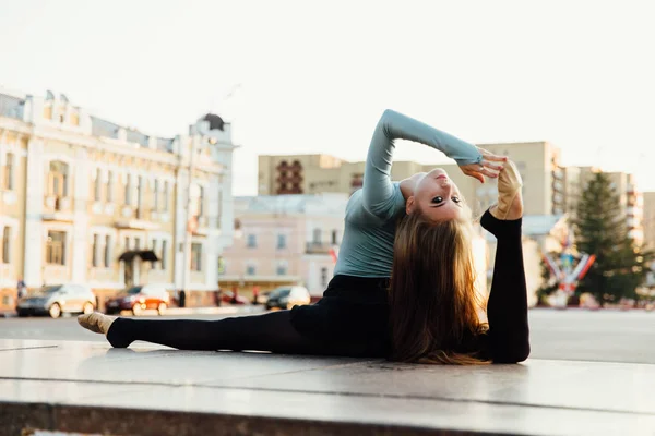 Bailarina sentado em pose ginástica no meio da rua da cidade. edifícios fundo . — Fotografia de Stock