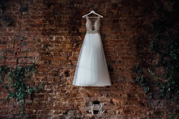 Lindo vestido de noiva pendurado em um cabide em uma parede de tijolo em um estúdio loft. Ninguém. . — Fotografia de Stock