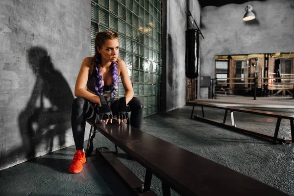 Fitness menina relaxante sentado no banco da escola de esportes depois de um treinamento de boxe duro . — Fotografia de Stock