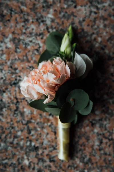 boutonniere, button hole flower, a cream peonies on granite table.
