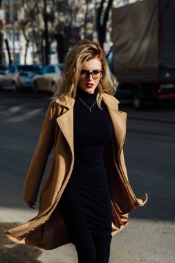 Moda Genç Kız bardaklarda. Sarışın, kırmızı dudaklar, bej kat şehir cadde boyunca yürüyüş.