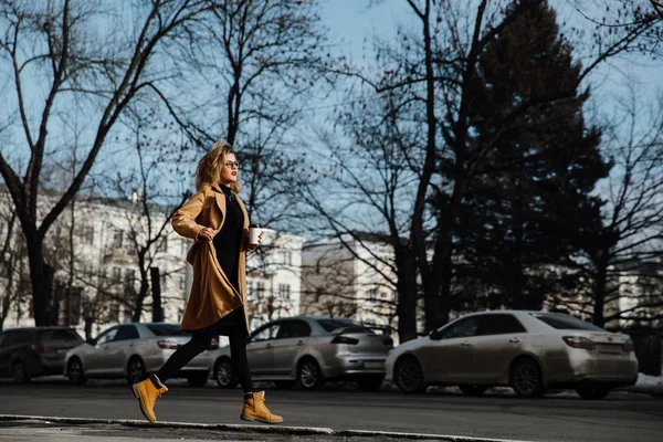 Chica de moda en un abrigo beige y una taza de papel de café en sus manos . — Foto de Stock