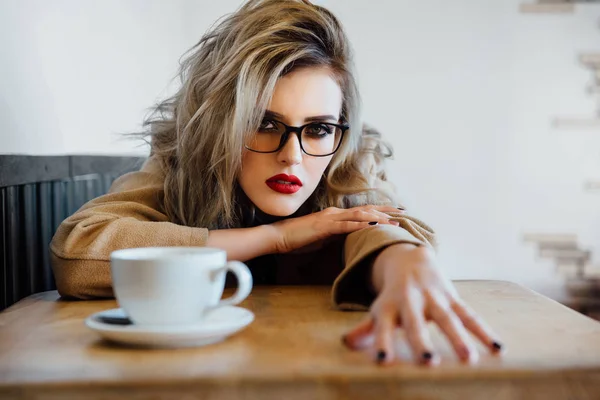 Beautiful fashionable stylish girl sits in a cafe with a cup of coffee. — Stock Photo, Image