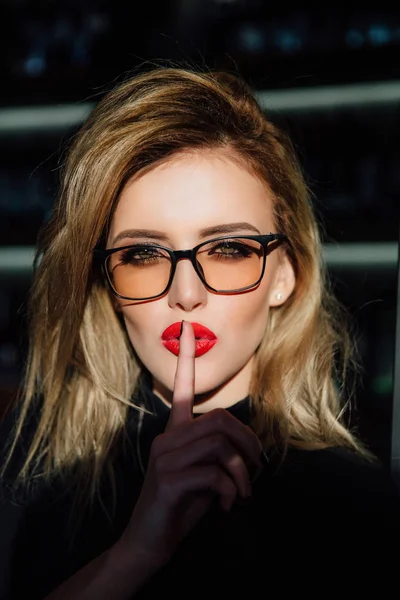 Hush. Woman in glasses ask for silence or secrecy with finger on red lips. shh hand gesture.