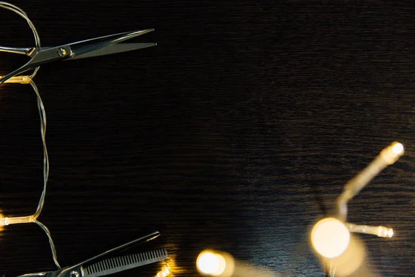Le forbici di parrucchiere professionali e una ghirlanda si trovano su un tavolo di legno nero . — Foto Stock