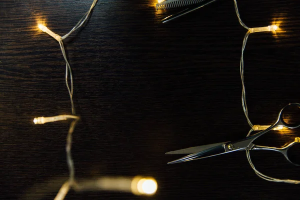 Le forbici di parrucchiere professionali e una ghirlanda si trovano su un tavolo di legno nero . — Foto Stock