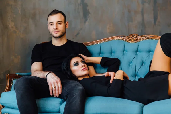 Giovane bella coppia in abiti scuri su un divano vintage turchese . — Foto Stock