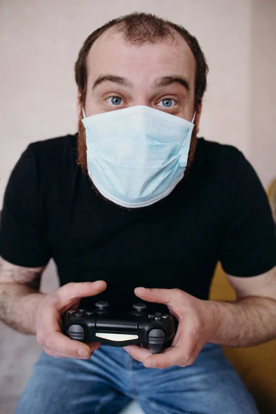 Łysy dorosły biały mężczyzna gra w gry wideo z maską medyczną na twarzy podczas kwarantanny Covid-19 Obrazy Stockowe bez tantiem