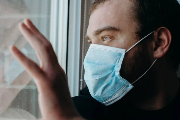 Coronavirus. Corona virüsünün hasta adamı pencereden bakıyor ve maske takıyor..