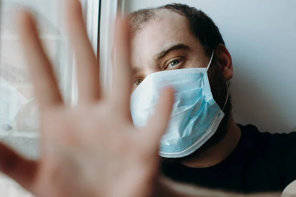 Coronavirus. Hombre enfermo de virus corona mirando a través de la ventana y usando protección antifaz . Imágenes De Stock Sin Royalties Gratis