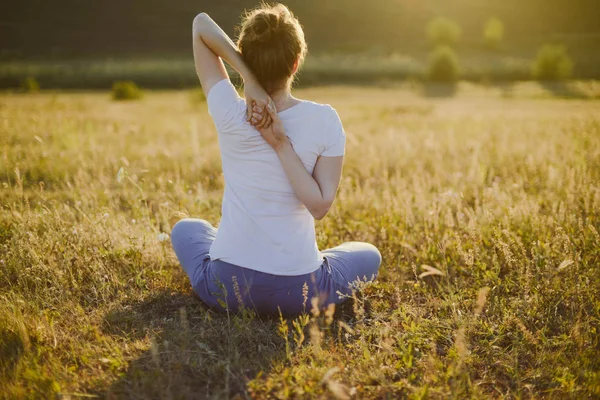 Ung kvinna sitter i namaste yoga pose med staden på bakgrunden. F — Stockfoto