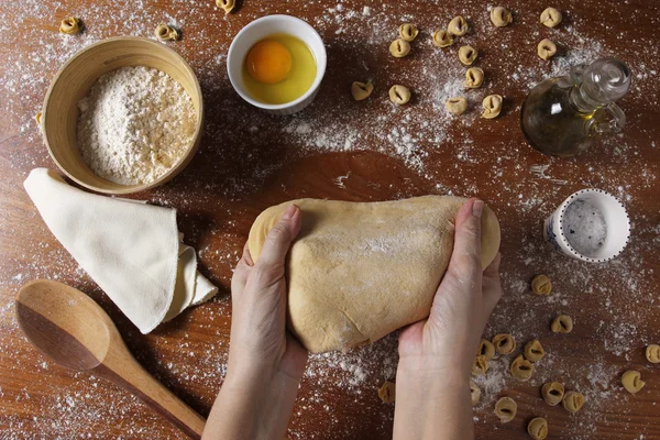 Manos femeninas amasando masa sobre mesa de madera con ingredientes — Foto de Stock