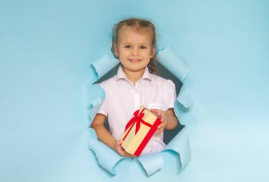 Güzel bir kızın kafası gazetedeki bir delikten dışarı bakıyor. Elinde kırmızı kurdeleli bir hediye tutan kız. Mavi arka plan. Şenlikli Noel kompozisyonu.