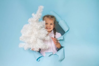 Güzel bir kızın kafası gazetedeki bir delikten dışarı bakıyor. Elinde kırmızı kurdeleli bir hediye tutan kız. Mavi arka plan. Şenlikli Noel kompozisyonu.