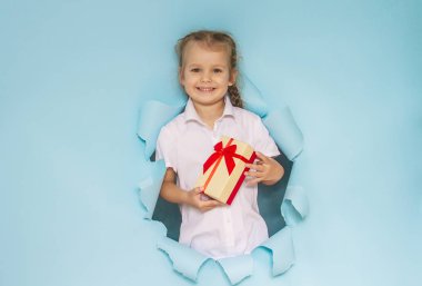 Güzel bir kızın kafası gazetedeki bir delikten dışarı bakıyor. Elinde kırmızı kurdeleli bir hediye tutan kız. Mavi arka plan. Şenlikli Noel kompozisyonu.