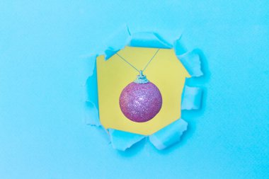 Mavi kağıt deliğinde pembe bir Noel balosu görülebilir. Üç boyutlu kompozisyon. Yeni yıl ve doğum günü konsepti. Metin için boş boşluk. 