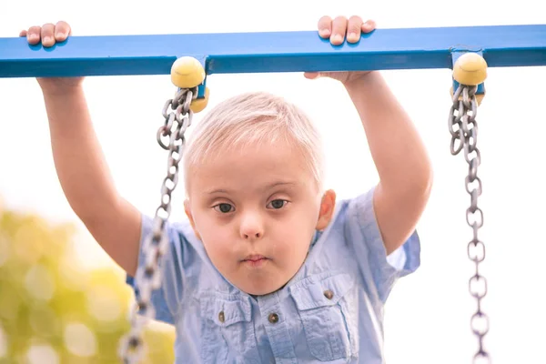 障害のある子供の日常生活 遊び場ではダウン症候群の少年が遊んでいます 赤ちゃんの染色体と遺伝性障害 — ストック写真