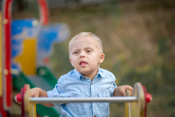 The daily life of a child with disabilities. A boy with Down Syndrome is playing in the playground. Chromosomal and genetic disorder in the baby.