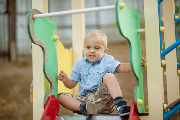 障害のある子供の日常生活 遊び場ではダウン症候群の少年が遊んでいます 赤ちゃんの染色体と遺伝性障害 — ストック写真