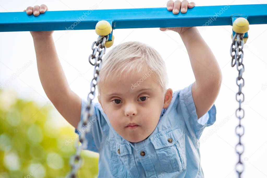 The daily life of a child with disabilities. A boy with Down Syndrome is playing in the playground. Chromosomal and genetic disorder in the baby.