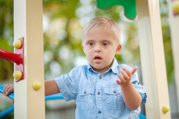 The daily life of a child with disabilities. A boy with Down Syndrome is playing in the playground. Chromosomal and genetic disorder in the baby.