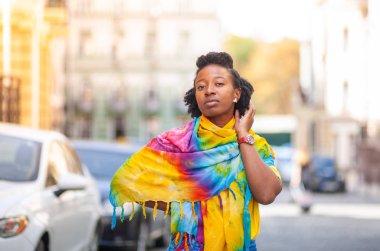 Güzel bir Afro-Amerikalı kız, parlak sarı bir şalla bir şehir caddesinde duruyor..