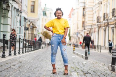 Hayat tarzı sokak kızı. Sarı tişörtlü ve kot pantolonlu Afrikalı Amerikalı kız.