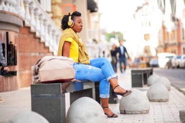 Hayat tarzı sokak kızı. Sarı tişörtlü ve kot pantolonlu Afro-Amerikalı bir kız bir şehir caddesinde duruyor. Bir fotoğraf için güzel poz veren şık bir kadın. Çok tatlı ve pozitif..