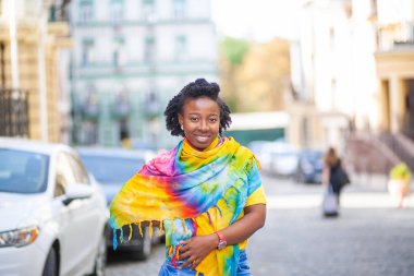 Güzel bir Afro-Amerikalı kız, parlak sarı bir şalla bir şehir caddesinde duruyor..