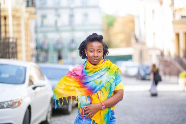 Güzel bir Afro-Amerikalı kız, parlak sarı bir şalla bir şehir caddesinde duruyor..