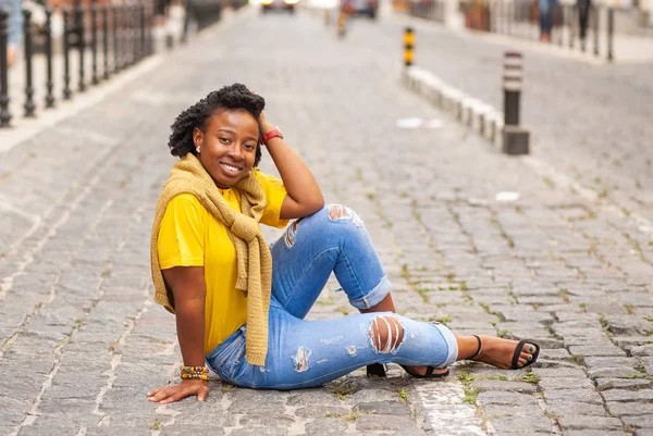 Lifestyle street girl. African American girl in a yellow T-shirt and blue jeans stands on a city street. Stylish woman posing beautifully for a photograph. She is very sweet and positive.