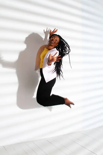 An African American girl in a blouse and jeans bounces high. Striped shadow on a white background.