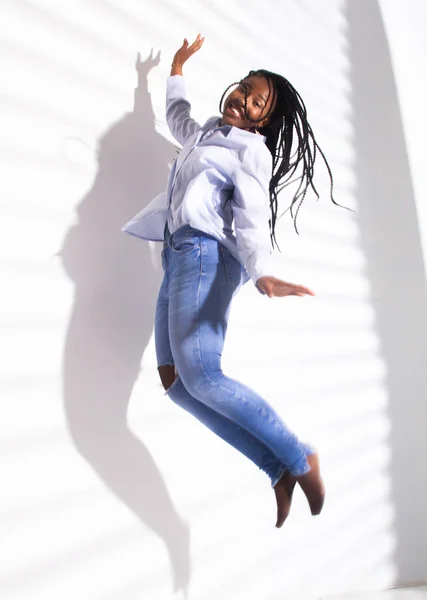An African American girl in a blouse and jeans bounces high. Striped shadow on a white background.