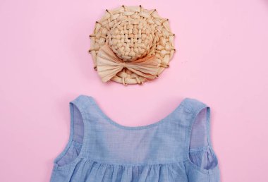 Pembe arka planda hasır şapka ve bebek mavisi bir elbise..