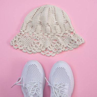 Pembe arka planda beyaz spor ayakkabılar ve panama.