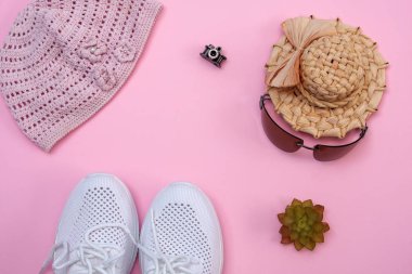 Güneş gözlüğü, hasır şapka, pembe arka planda beyaz spor ayakkabılar. Güzel, yumuşak, düz.