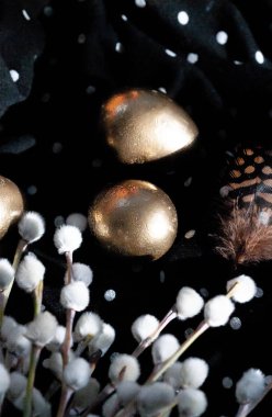 Paskalya tatili, karanlık bir arka planda kompozisyon. Altın yumurta ve siyah kumaşlı keklik tüyleri..