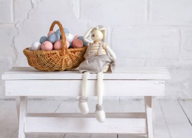 Paskalya tavşanı pastel çiçekli bir sepetin yanında oturur. Paskalya yumurtaları. Dini bahar tatili.