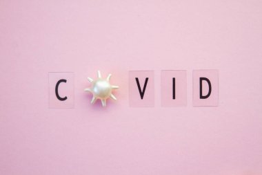 Koronavirüs salgını sırasında virüse benzer parçacıkların bulunduğu pembe bir arkaplanda siyah harflerle yazılmış renkli yazı..