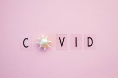 Koronavirüs salgını sırasında virüse benzer parçacıkların bulunduğu pembe bir arkaplanda siyah harflerle yazılmış renkli yazı..