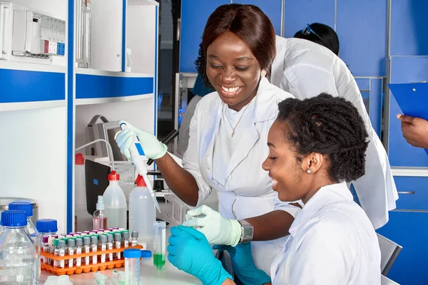 Testing facility. Young African female scientists or medical students, positive energetic smiling laughing women work together testing blood, nucleic acid and other medical tests for virus infections.