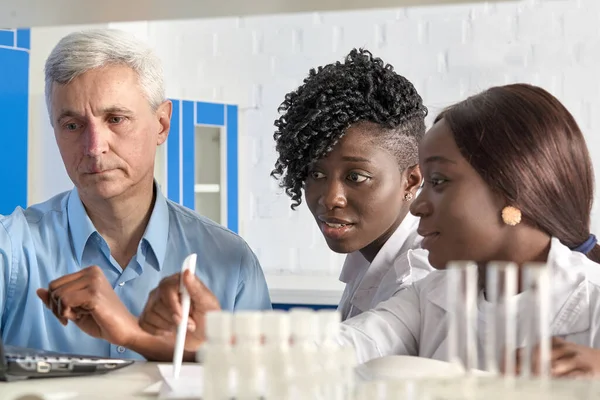 ヨーロッパのチームリーダーとアフリカの医療学生は 新しいコロナウイルス試験法の最適化について議論しています 上級白人男性と女性2人 — ストック写真