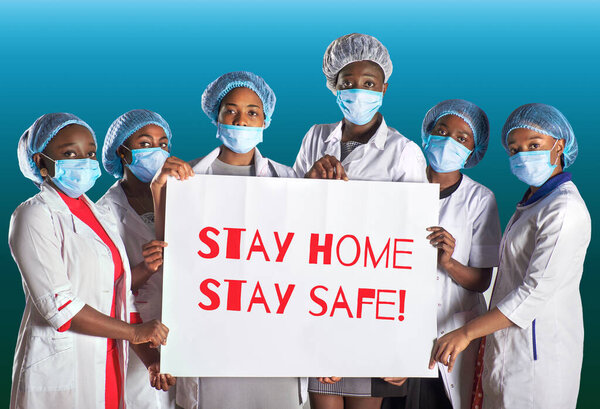 Group of African women nurses activists in face mask with hand placard. Text Stay home stay safe. Group of medics with message for public, information alert for coronavirus causing covid-19.