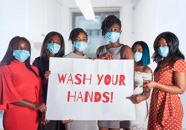 Group of African women nurses activists in face mask with hand sign placard with caption Wash your hands. Group of medics with message for public, information alert for coronavirus causing covid-19.