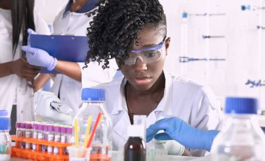 Araştırma laboratuvarında ya da tıbbi test laboratuvarında çalışan Afrikalı kadın tıp öğrencileri hastalar üzerinde çeşitli testler yapıyorlar. Kadın araştırmacılar PCR reaksiyonunun otomatik pipetle DNA 'yı güçlendirmesini sağlıyor..