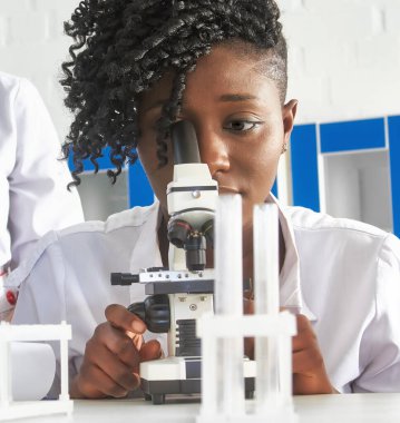 Genç ve çekici Afrikalı kadın bilim adamı, mezun ya da tıp öğrencisi test laboratuarı ya da üniversite biyoloji pratik kursunda hasta biyopsisi örneklerini mikroskopla gözlemler. Pratik anatomi kursu.